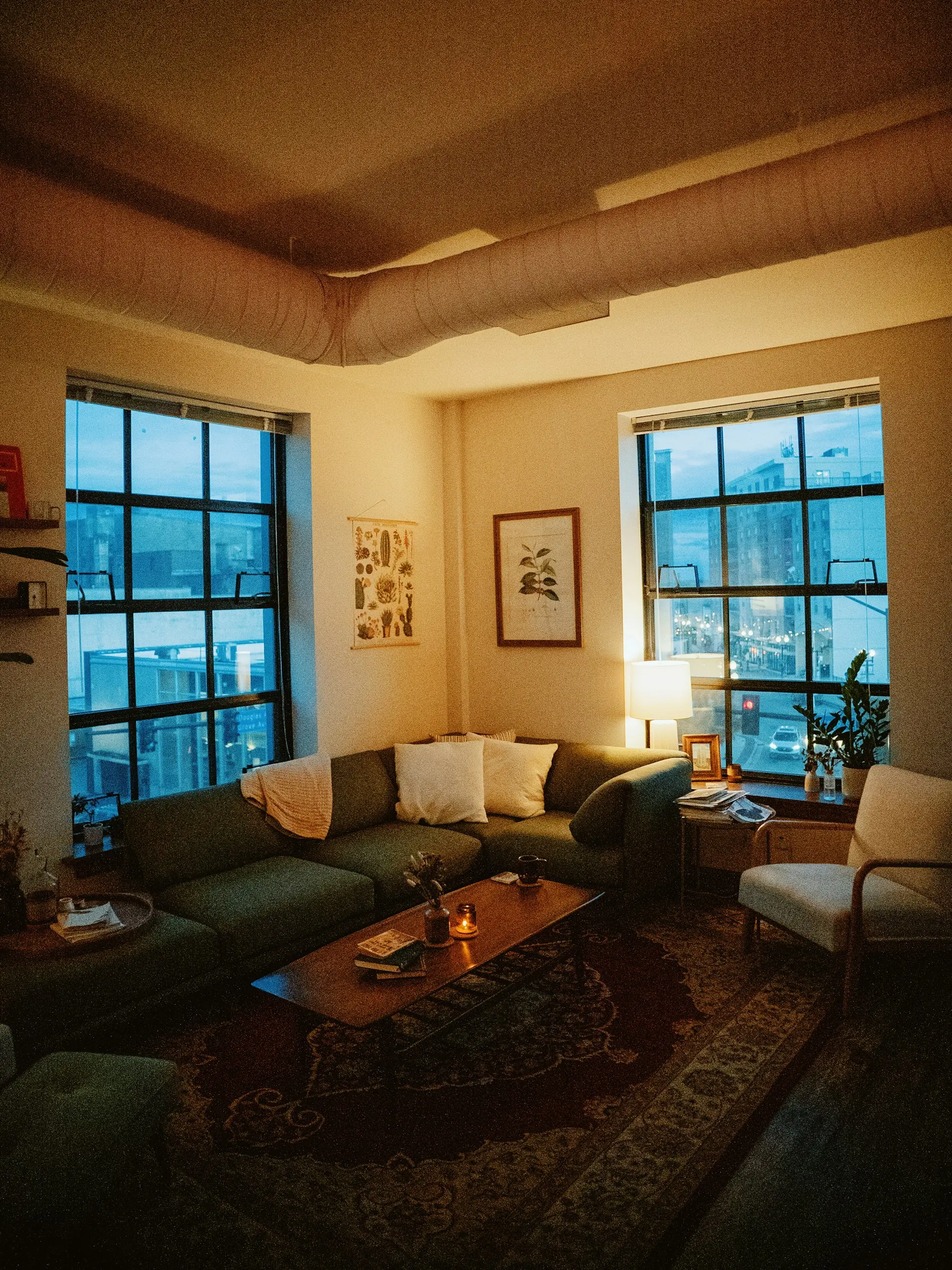 Gemütliches Wohnzimmer mit großen Sprossenfenstern und Lampenlicht am Abend